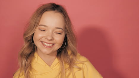 happy young woman in yellow hoodie smiling against pink background