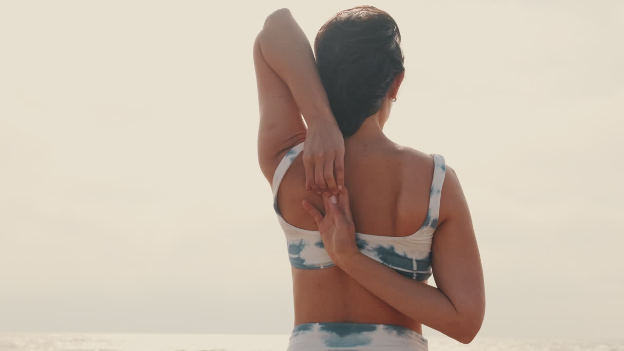 Donna che allunga spalle e braccia in posizione yoga in riva all'oceano