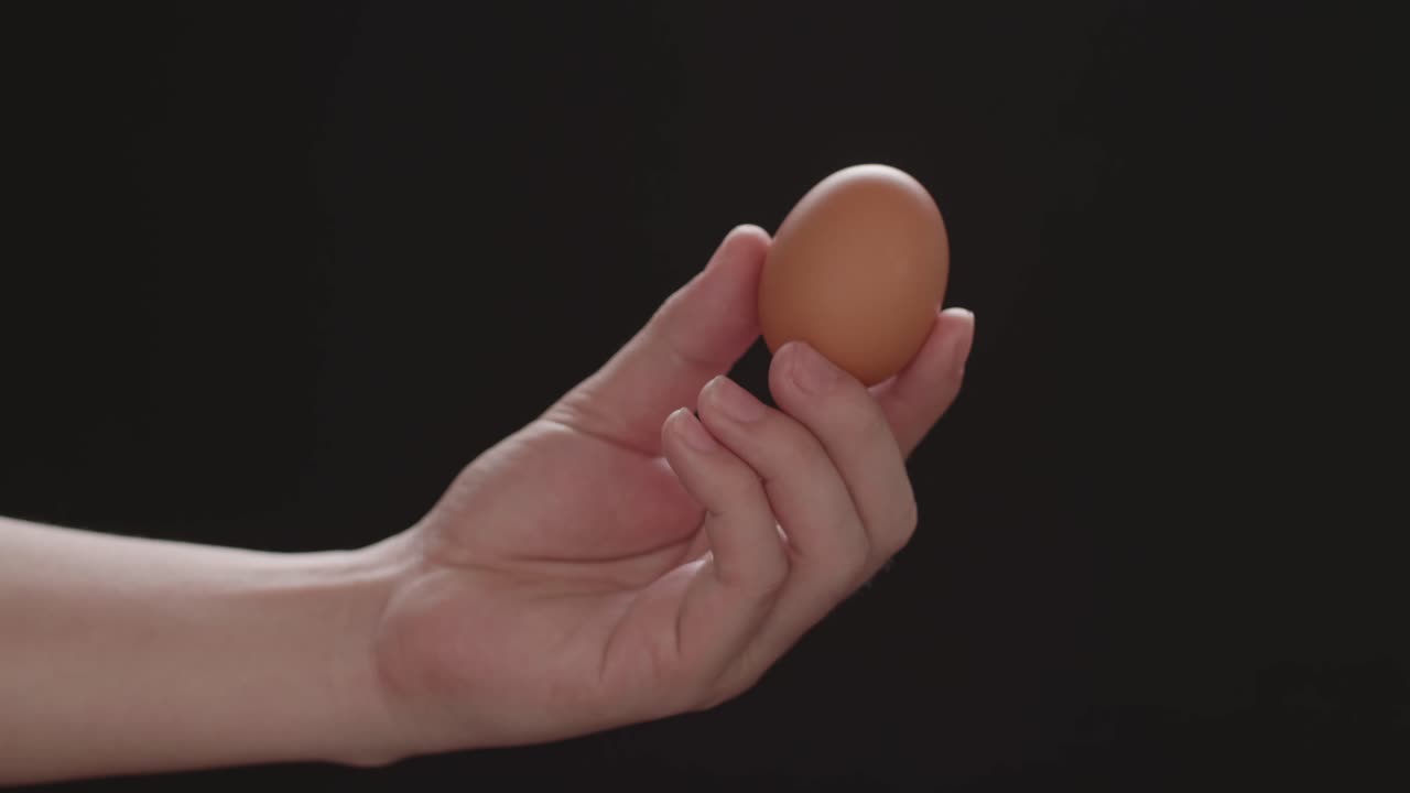 Hand Holds And Shows Brown Chicken Egg. Close-Up, Black Background