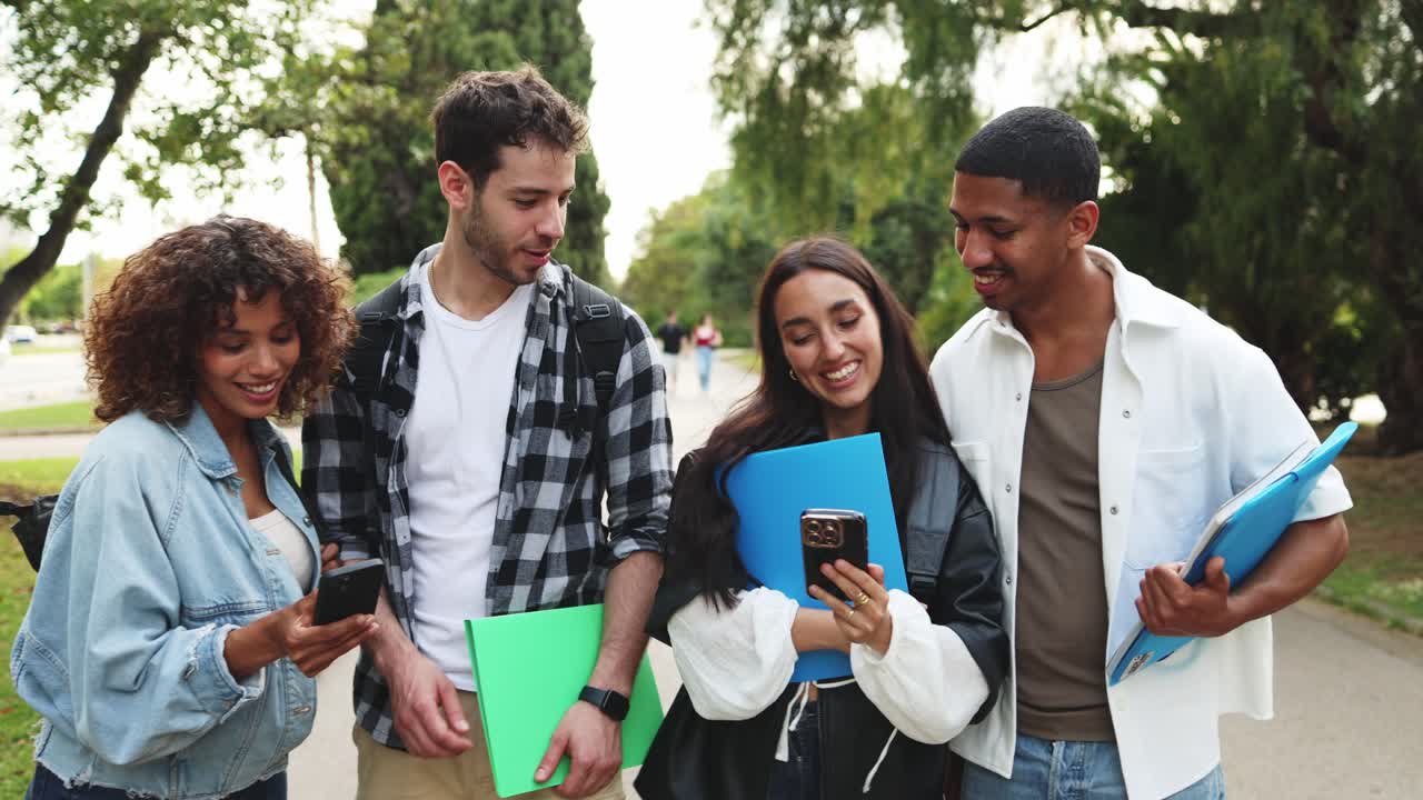 Glade flerkulturelle studenter bruker smarttelefoner og ler på campus