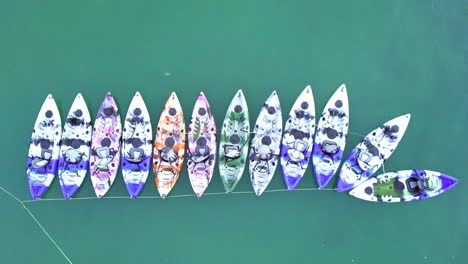 a dynamic top-down aerial shot of colorful kayaks or small watercrafts that are tied up neatly and ready to be rented by tourists