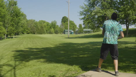 Un-Hombre-Ejecuta-Un-Poderoso-Drive-Durante-Un-Juego-De-Disc-Golf-En-Un-Amplio-Y-Soleado-Parque,-Mostrando-La-Energía-Y-Precisión-Del-Deporte