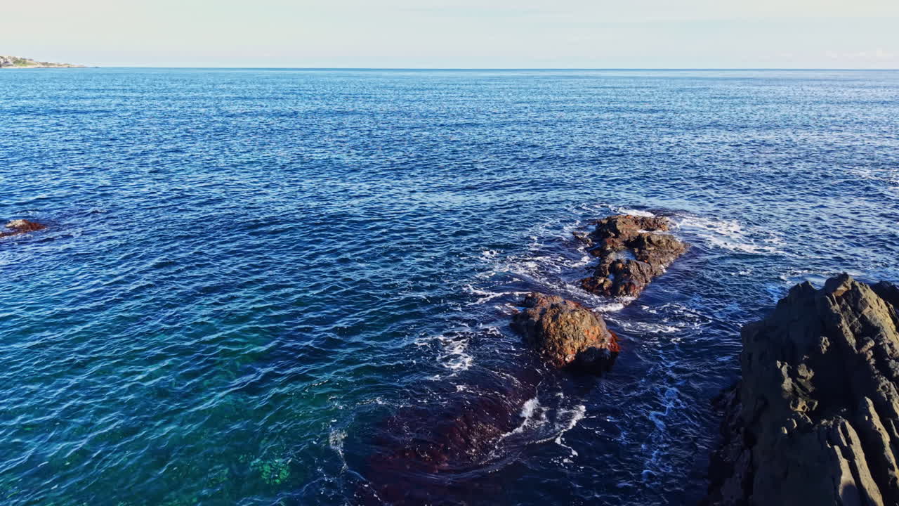 Serena vista costiera che mette in mostra onde vivaci e rocce frastagliate sotto un cielo limpido a mezzogiorno
