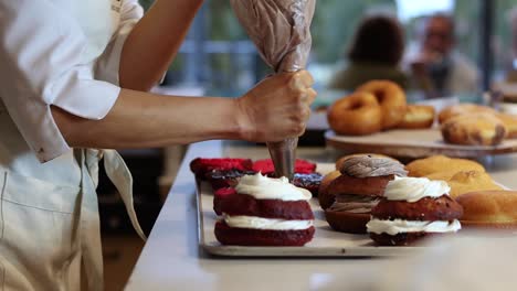 unrecognizable baker adding cream on cakes in kitchen