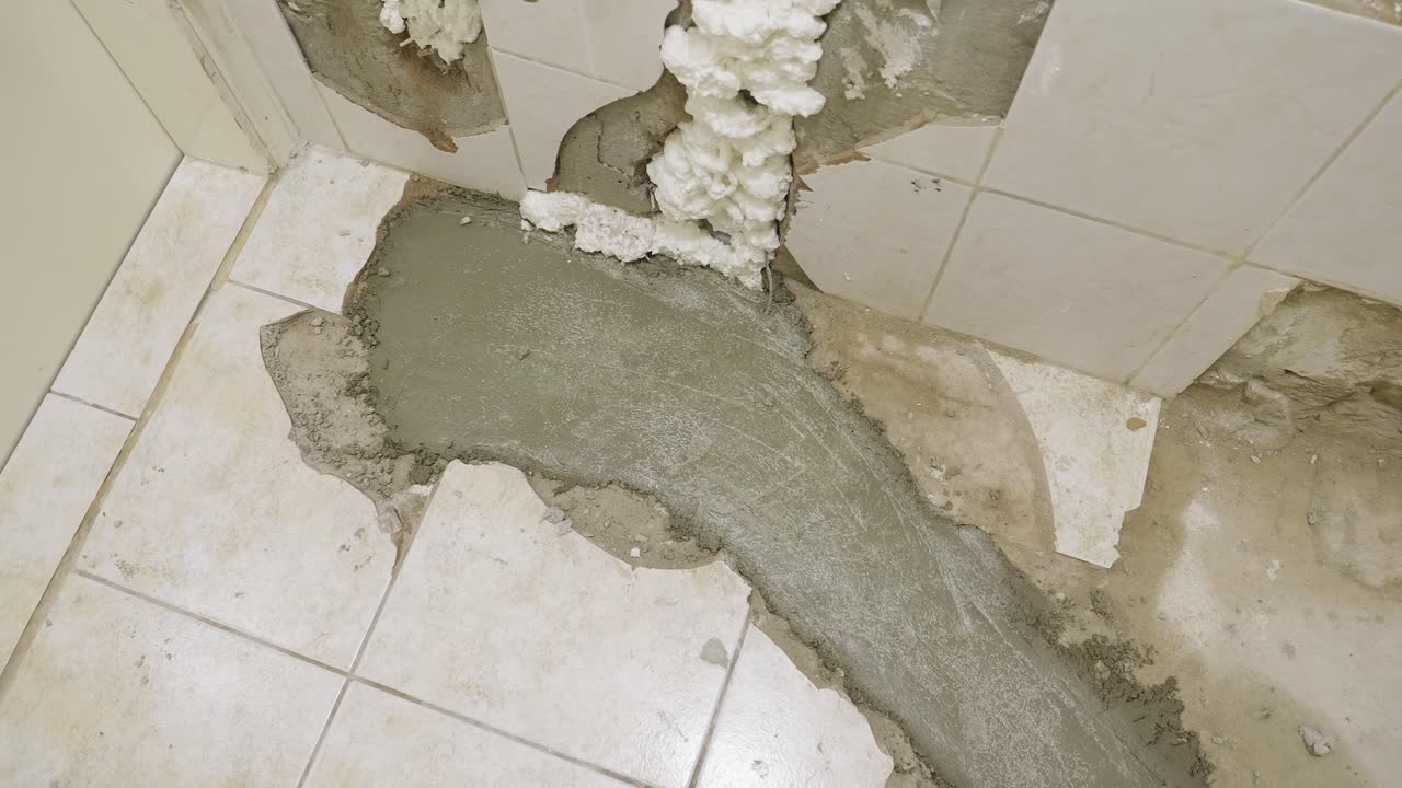 현재 전체 복원을 진행 중인 욕실 바닥의 클로즈업 샷, 배수 파이프가 교체되었고 젖은 콘크리트가 부어져 틈을 메우고 새 파이프를 보호했습니다.