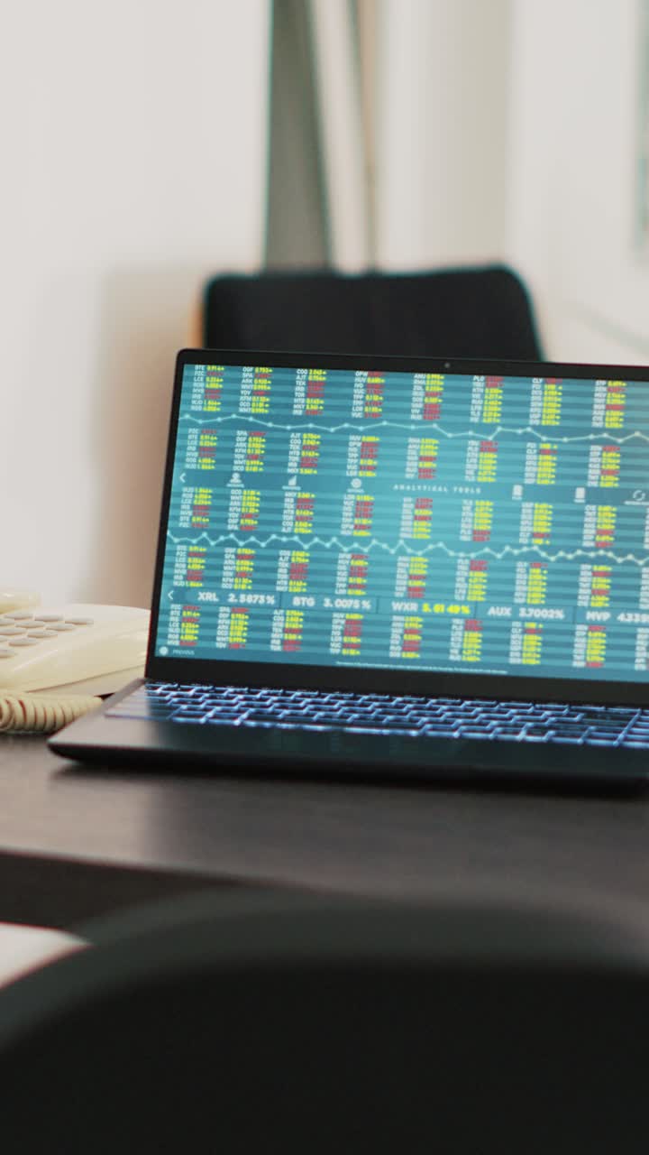 Vertical video Paperwork on desk next to laptop in office showing stock exchange values