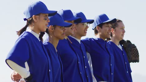 happy diverse team of female baseball players standing in line with arms around each other singing