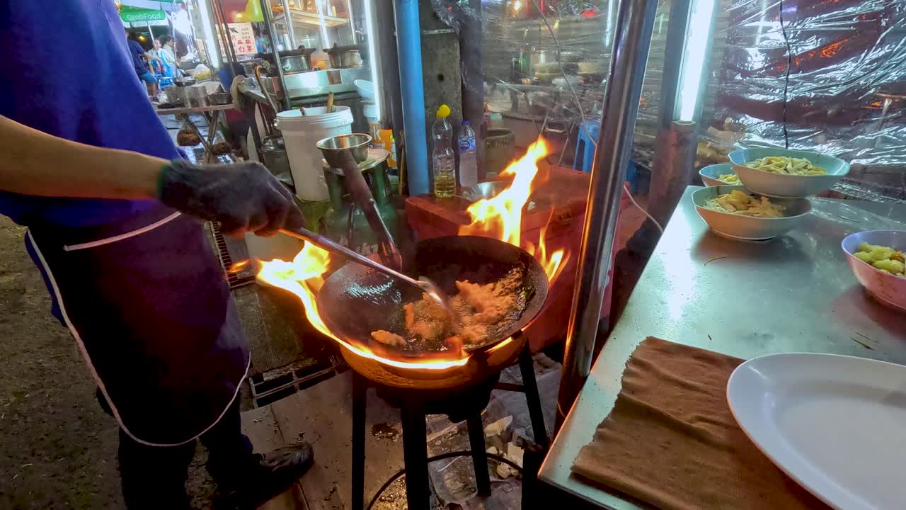 Chef stir-fries food in flaming wok at night street market, vibrant lighting, dynamic camera angle
