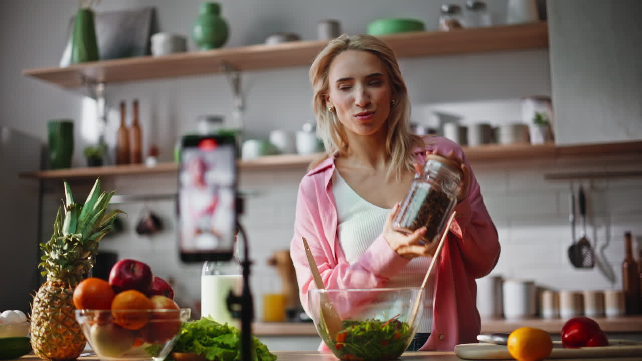 Primer plano de una bloguera gastronómica grabando un vídeo con un smartphone en la cocina. Chica contenta hablando.