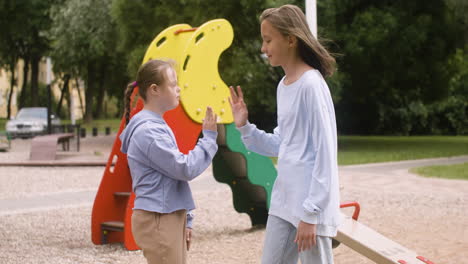 little girl with down syndrome giving high five another girl in the park on a windy day