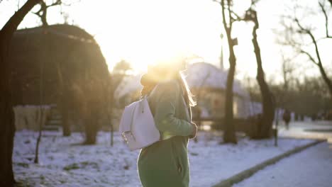 rare view of a woman walk by winter park, listening to music on the phone using headphones, looking back over the shoulder