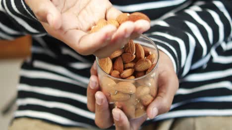 person eating almonds from a glass container