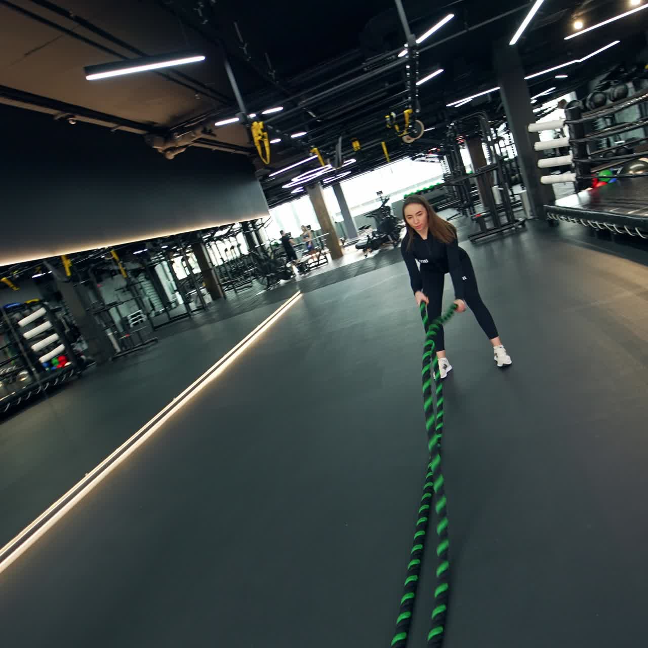 Young woman doing exercise with long ropes in the sport gym. Fit lady in black sport suit training in an empty sports club