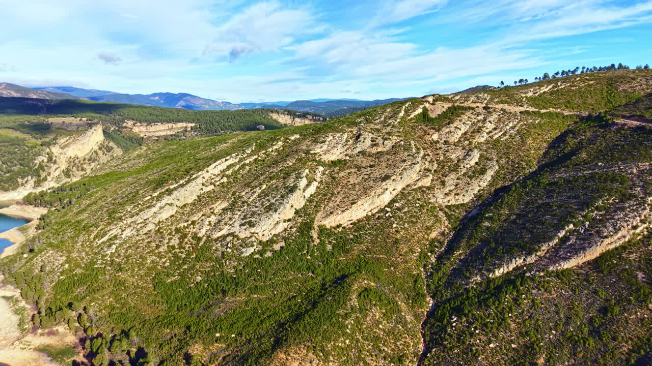 Utsikt over et fjellandskap ved en innsjø, med grønne åser og klar blå himmel, fanget i ettermiddagslyset på en solrik dag i et landlig område.