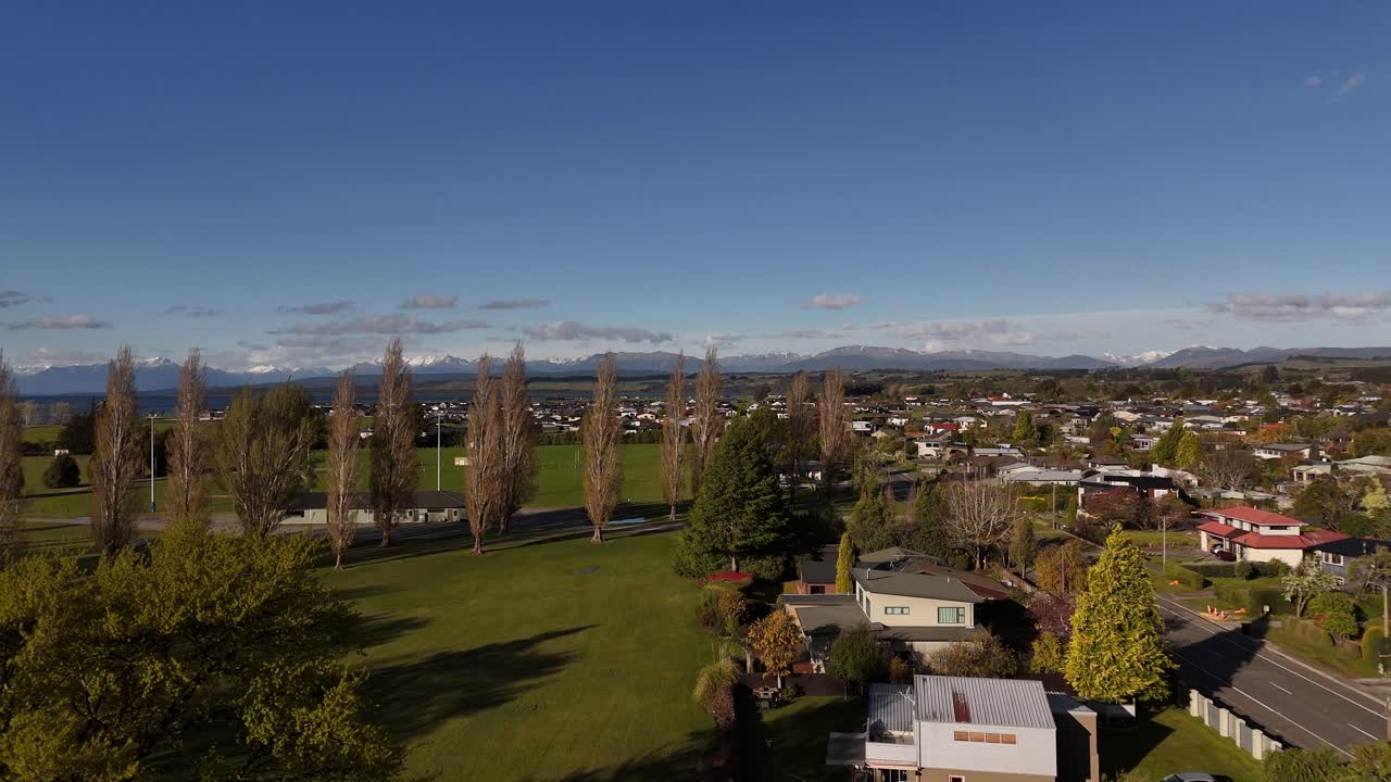 Scenic 4K aerial drone footage rising over a park with autumn trees on the shore of Lake Te Anau. Majestic view of blue water and Fiordland mountains on New Zealand's South Island