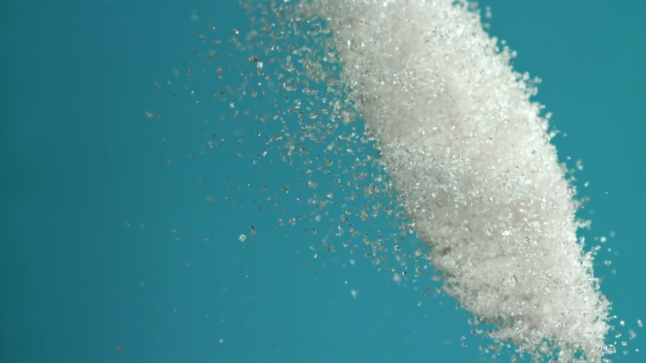 Flusso al rallentatore di zucchero bianco che cade su uno sfondo blu.