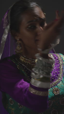 vertical video close up of female kathak dancer performing dance wearing traditional indian dress seated on floor in spotlight