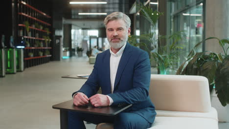 happy middleaged caucasian businessman looking at camera and waving hand hello in office lobby