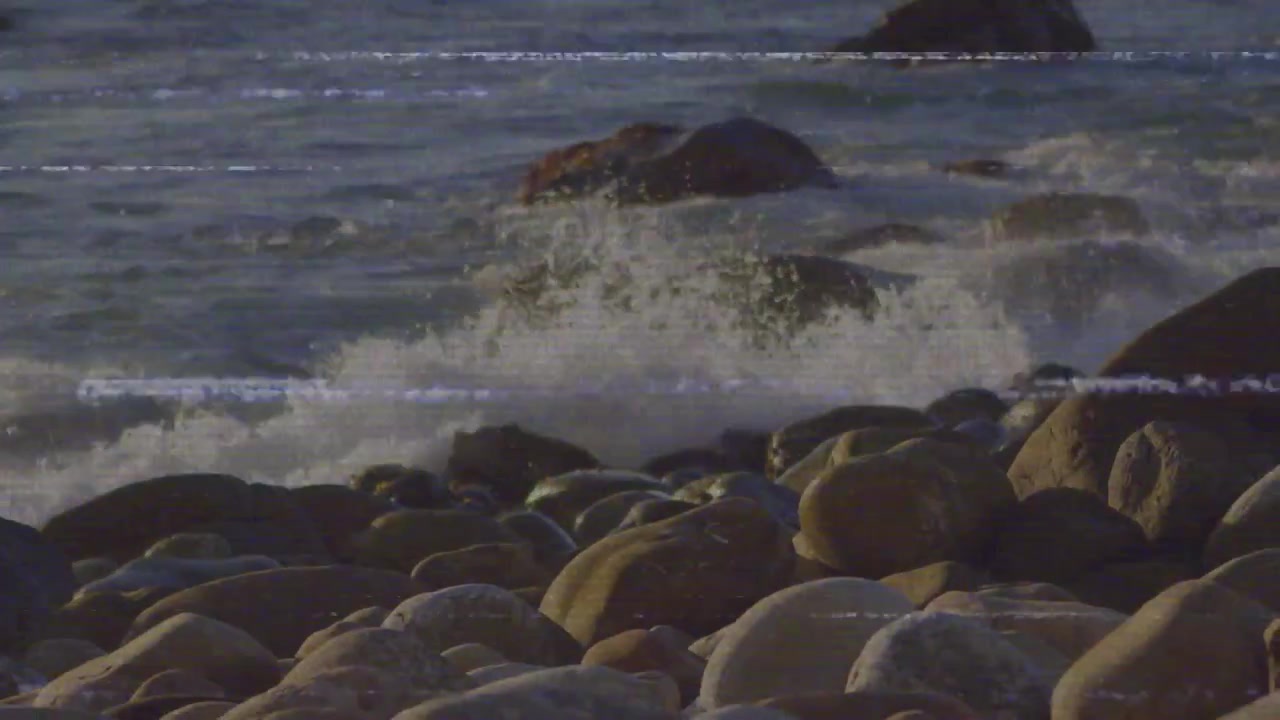 Mareggiata che sale, spingendo le onde a infrangersi su uno sperone roccioso, spruzzando schiuma sui massi in un ciclo ritmico.