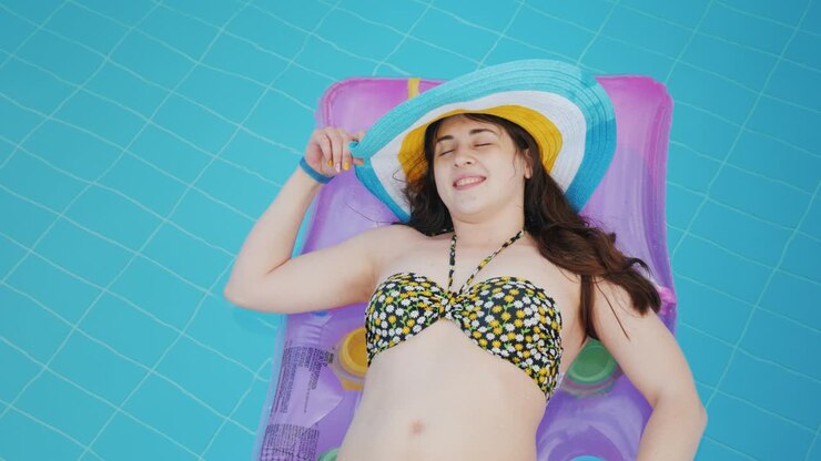 A pretty tourist woman swims on the mattress by the pool, rests, enjoys a vacation