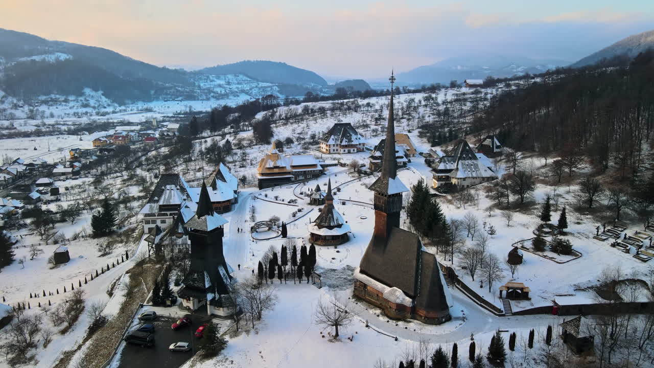 Letecký dronový pohled na klášter Barsana v Rumunsku. Hlavní kostel a další budovy, kopce pokryté holým lesem a sněhem, zima