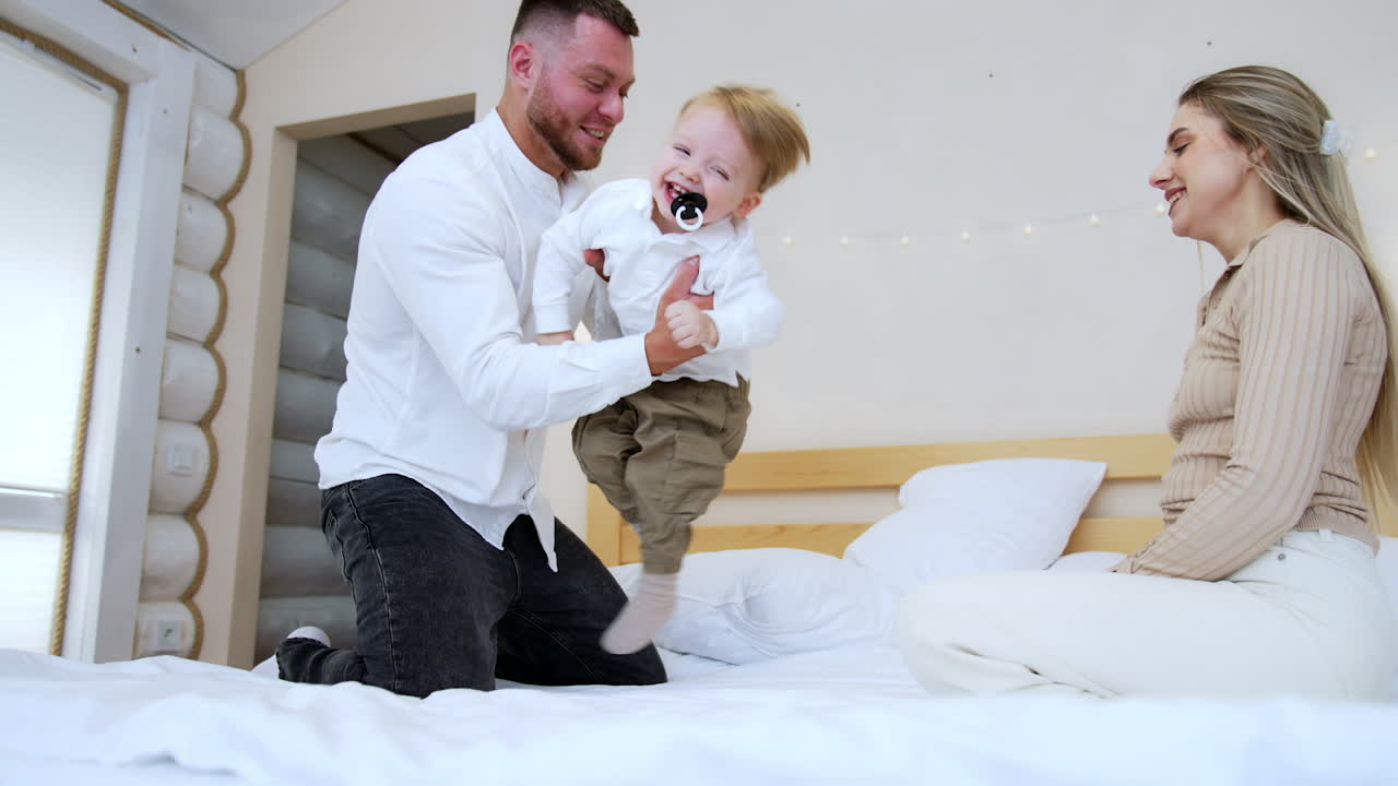 Young Caucasian parents play together with their child. Mom and dad tumble their son on the bed. Low angle view.