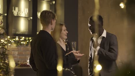 Group friends wearing stylish clothes while talking and holding champagne glasses at new year&#039;s party