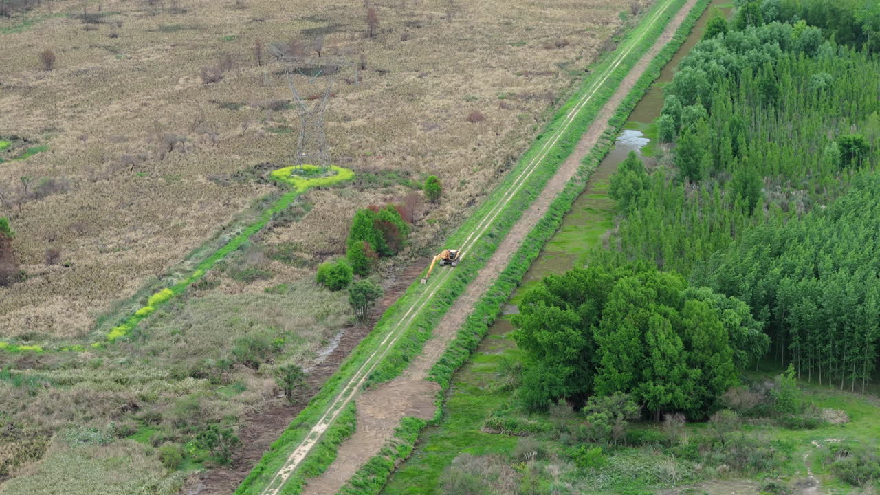 Excavator working on edge of green field in rural Argentina moving earth for land clearing, panoramic aerial