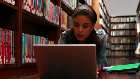 estudiante acostado en el suelo en la biblioteca usando una computadora portátil
