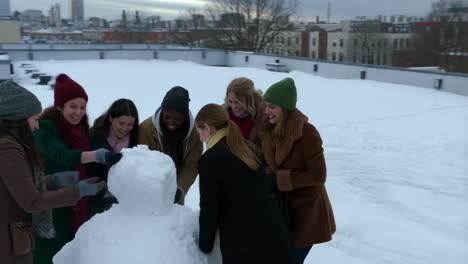 women building a snowman on a snowy rooftop