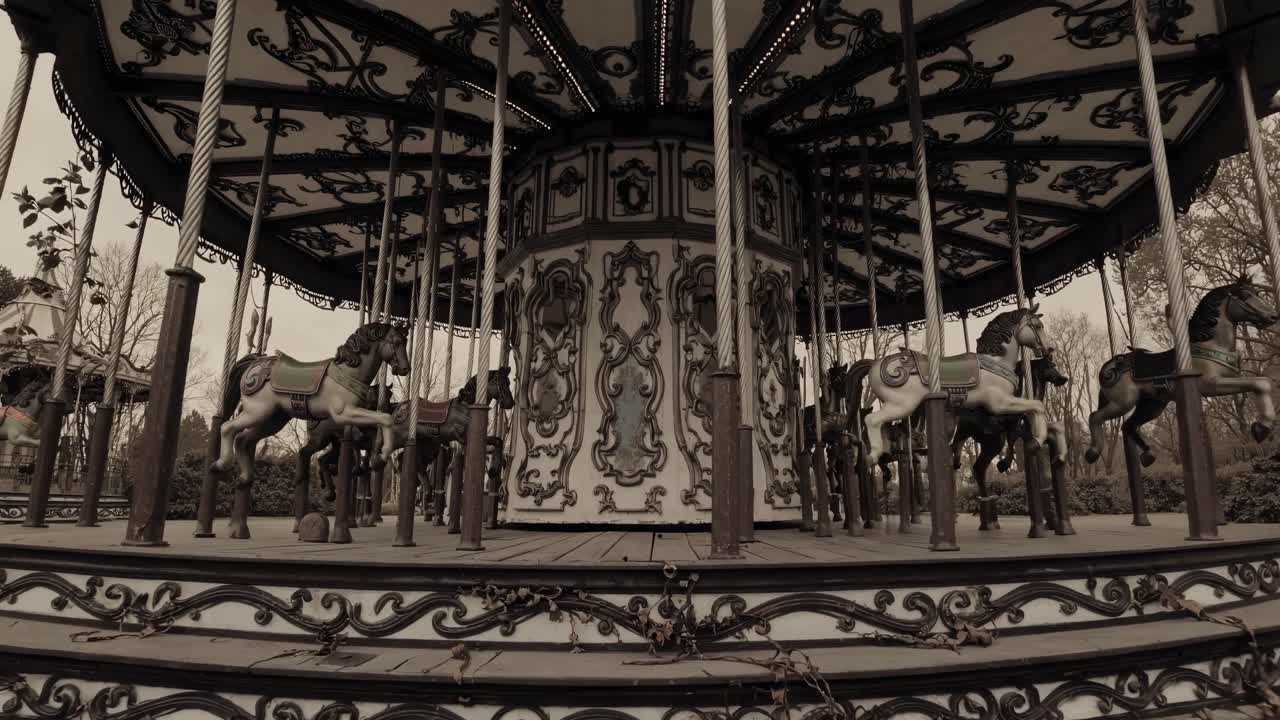 Fotogramma video color seppia di un vecchio carosello, ripreso da un'angolazione bassa, che mette in risalto intricate lavorazioni in ferro.