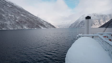 POV-video-of-a-ferry-ride-through-Geirangerfjord-in-winter,-featuring-stunning-views-of-snow-covered-mountains,-a-bright-sky,-and-reflections-in-the-fjord