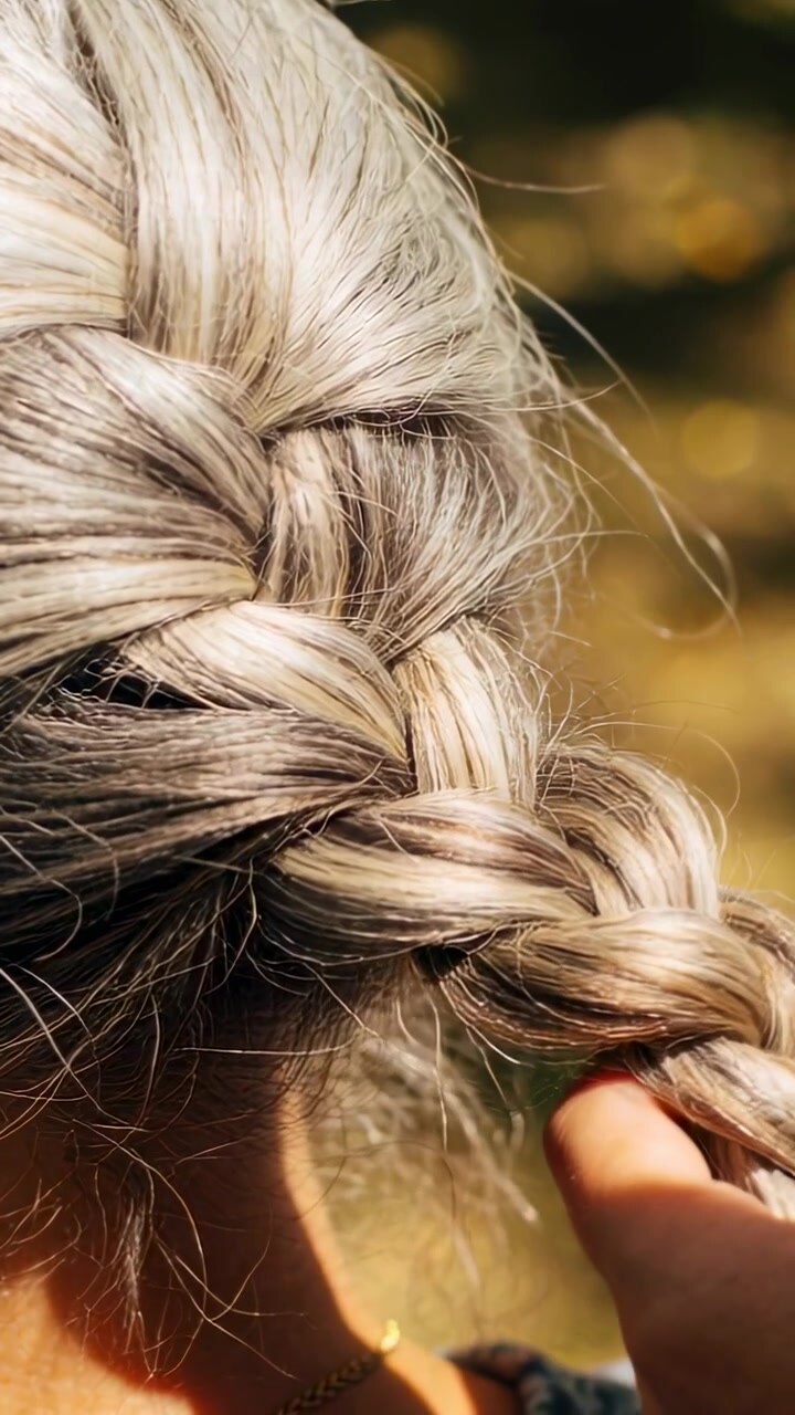 Video verticale: Una mano destra che entra e sistema la treccia di una donna verso il basso in una sfocatura calda, mostrando i capelli ribelli.