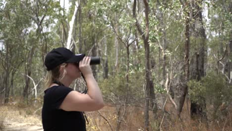 blonde girl wearing hat looking through binoculars brushing flies away