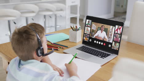 schoolboy using laptop for online lesson at home, with diverse teacher and class on screen