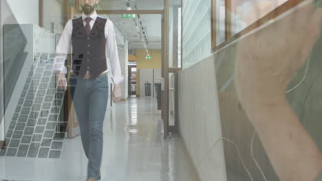 animation of hands of man using laptop with businessman walking in workplace corridor