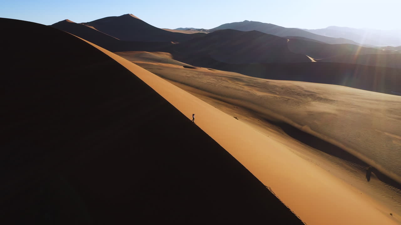 Drone shot of a around a photographer standing on a dune, taking pictures of the Namib desert, golden hour in Namibia