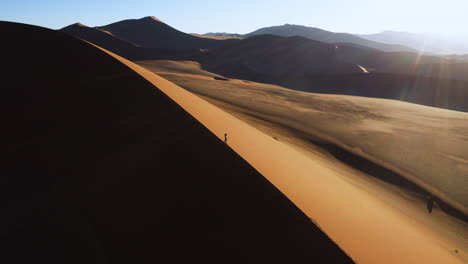 drone shot of a around a photographer standing on a dune, taking pictures of the namib desert, golden hour in namibia