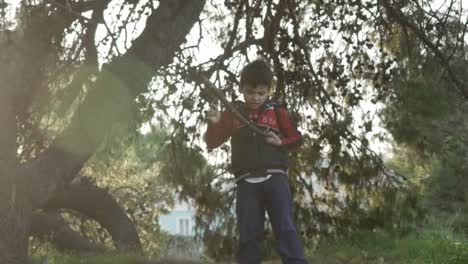 caucasian boy playing with wooden sticks of tree's branch in the forest, sun flares on screen 120fps