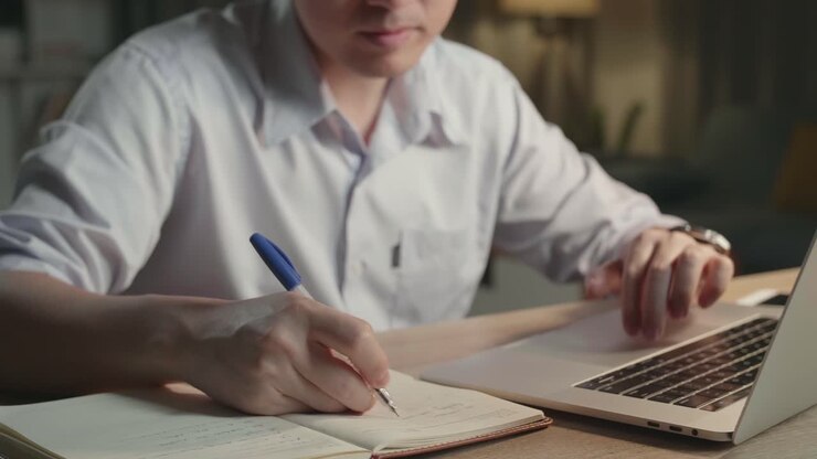 Persona che lavora di notte con laptop e quaderno.