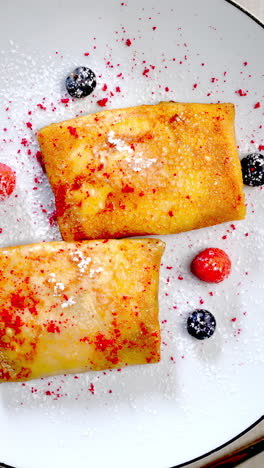 ukrainian traditional nalysnyky featuring forest berries, powdered sugar, and orange juice served on white plate with refined gourmet presentation