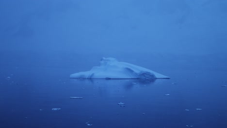 iceberg at night floating in ocean in antarctica, close up blue iceberg in dark moody scene in antarctic peninsula sea water in winter seascape, iceberg detail in icy scenery