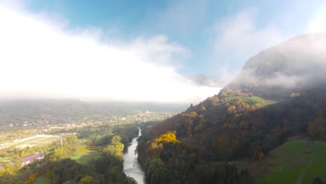 stunning view of mountain cliffs hiding in the clouds, separated by clear fresh water river in the morning of a late autumn day