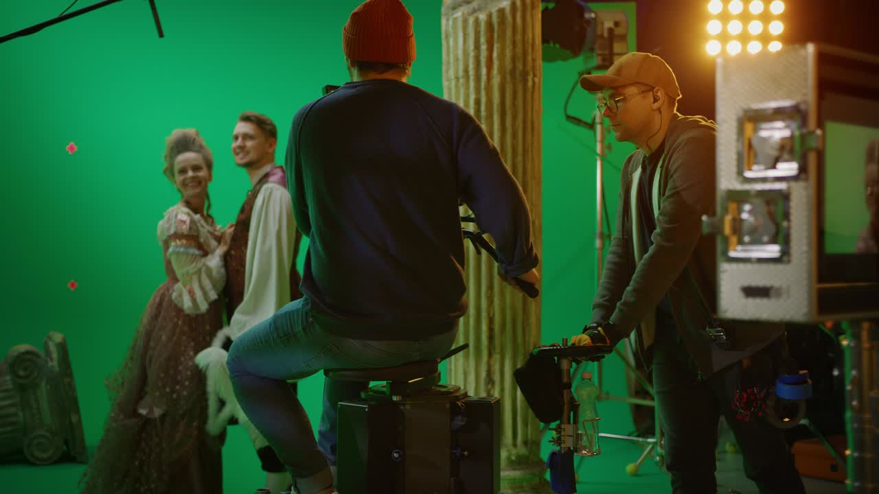 en el set del estudio de cine filmando una escena de pantalla verde de una película histórica. el camarógrafo en el tranvía del ferrocarril filmando a dos actores disfrazados mientras el director controla el proceso. equipo profesional en la realización de películas de gran presupuesto