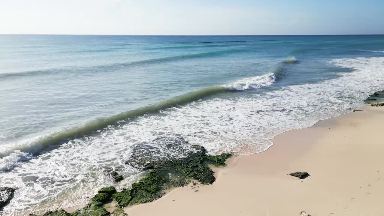 Vue aérienne des vagues calmes des Caraïbes déferlant sur la plage de sable de Xcalacoco au Mexique, avec une eau claire, de légères vagues et des paysages côtiers paisibles capturés par une prise de vue ascendante d’un drone.