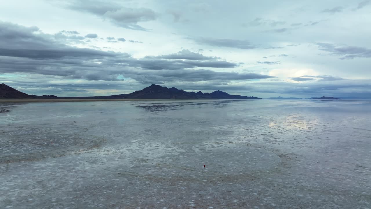 Wide Aerial drone trucking left shot of the famous Bonneville Salt Flats in Utah near Wendover, Nevada flooded from rain, creating mirage reflections with mountains on a stormy spring evening