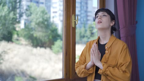 christian young woman praying in front of the window.