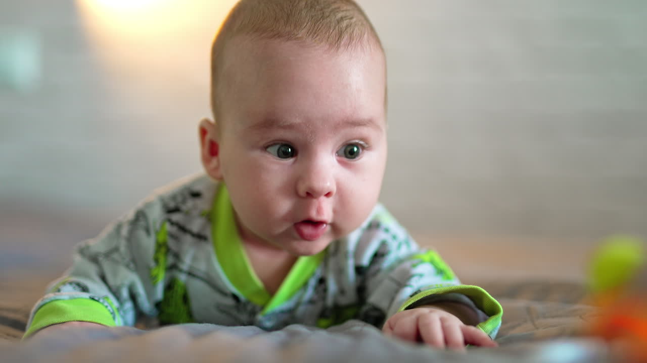Beautiful baby boy lies on the bed and strives to get a toy in front of him. Portrait of a child interested in a bright thing. Close up.