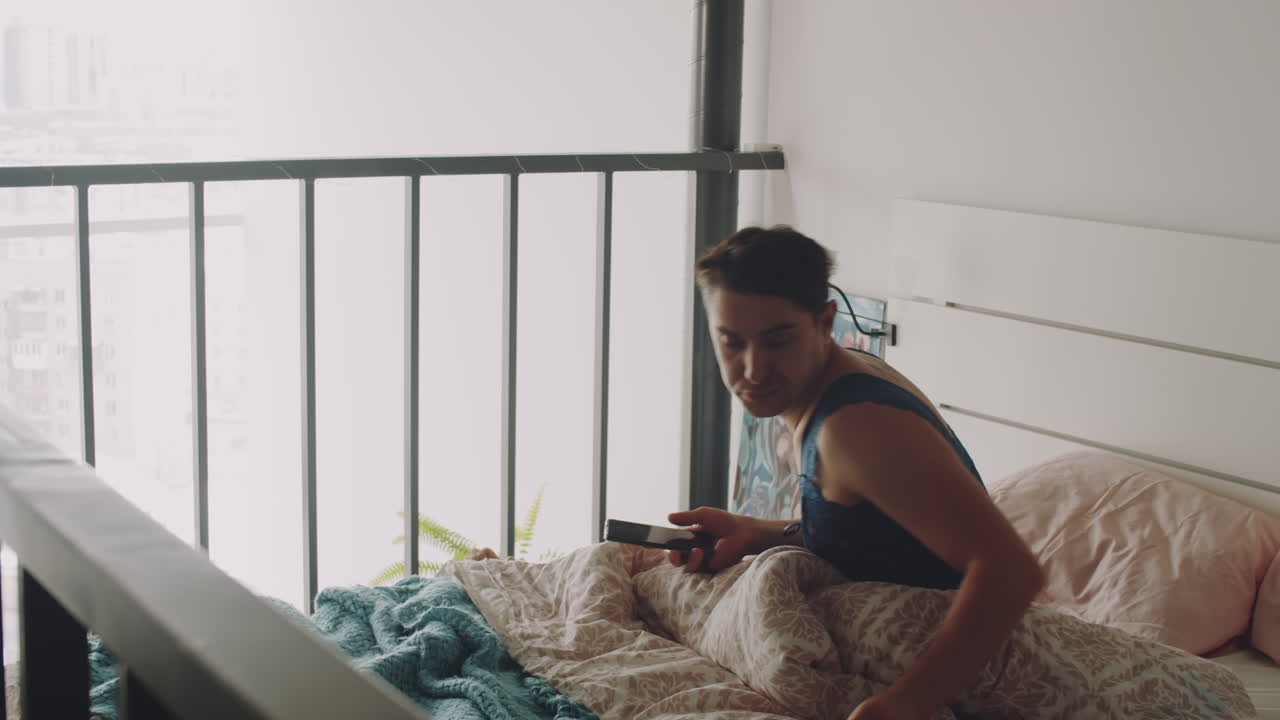 hombre transgénero despertando y hablando por teléfono por la mañana en casa