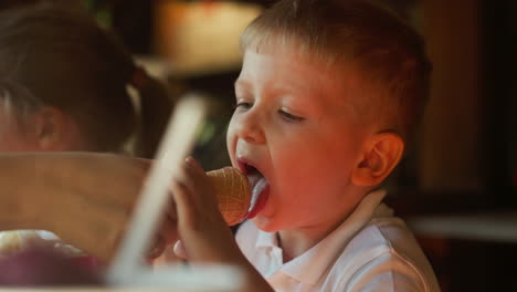 un niño pequeño lame el helado de chocolate sostenido por la mano de la madre en una cafetería a cámara lenta.
